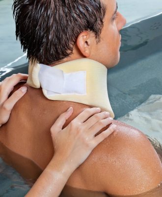 Young man wearing neck brace being massaged by female while sitting in pool