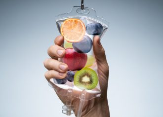 Person's Hand Holding Saline Bag Filled With Various Fruit Slices Against Grey Backdrop